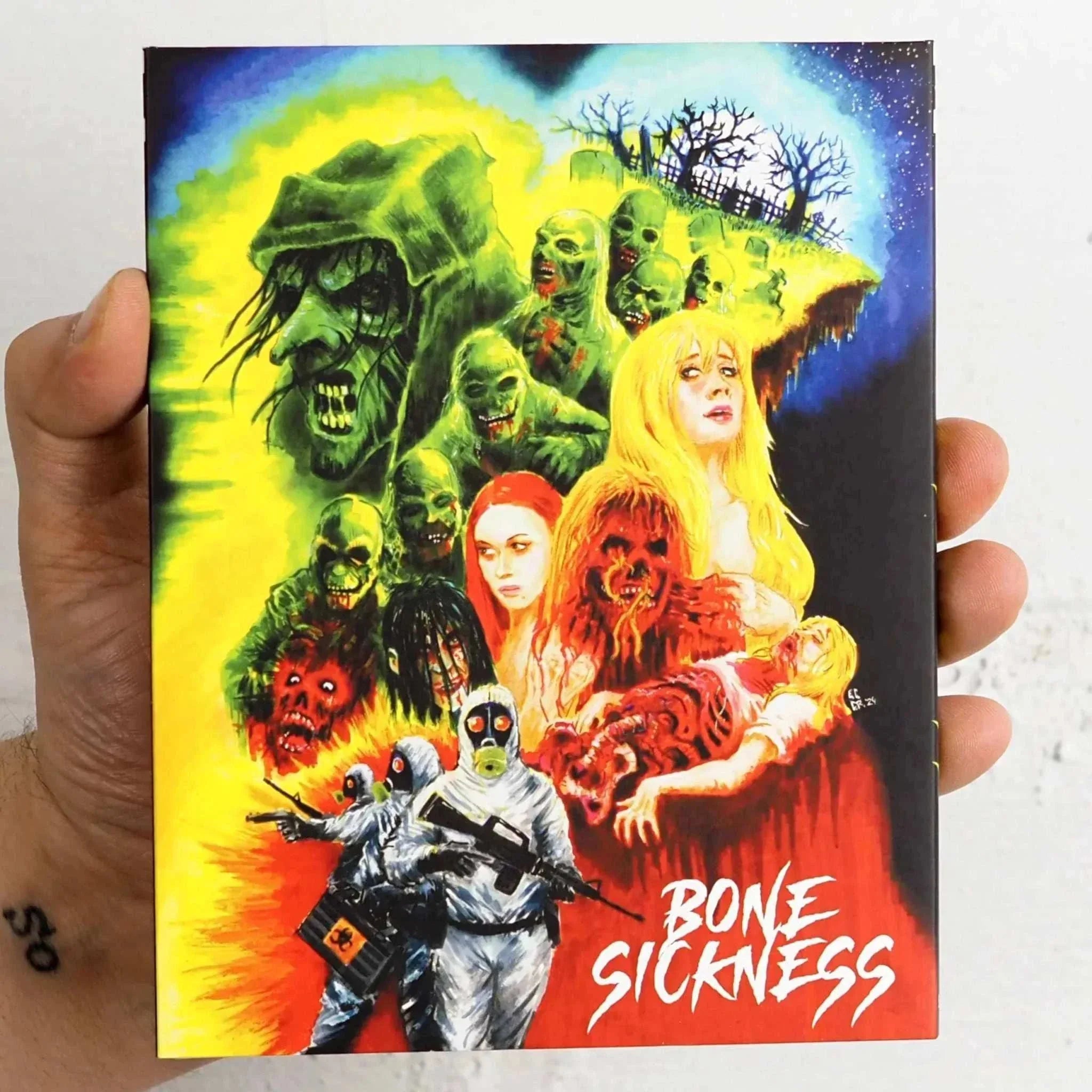 Hand holding Saturn's Core - Bone Sickness Blu-Ray slipcover featuring vibrant horror artwork with zombies and characters.