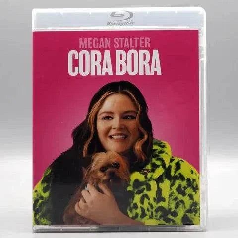 Blu-Ray cover of "Cora Bora" featuring Megan Stalter holding a small dog, vibrant pink background.