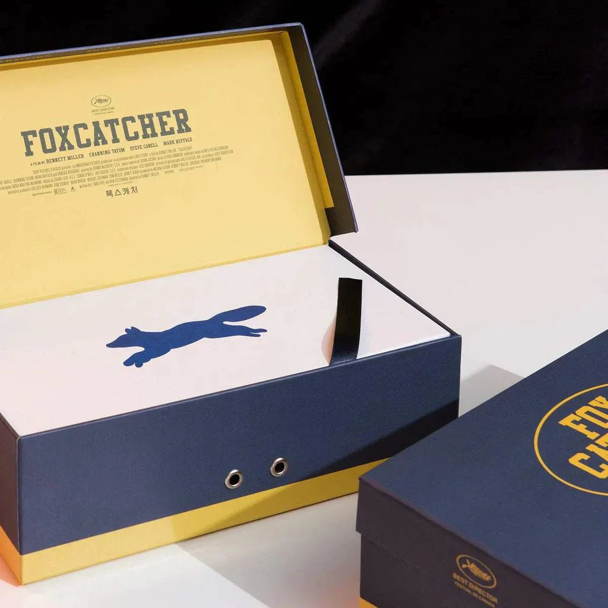 Foxcatcher Deluxe Box Blu-ray Steelbook with exclusive artwork, gold medal replica, gym towel, poster cards, essay book, and shooting script in protective deluxe packaging