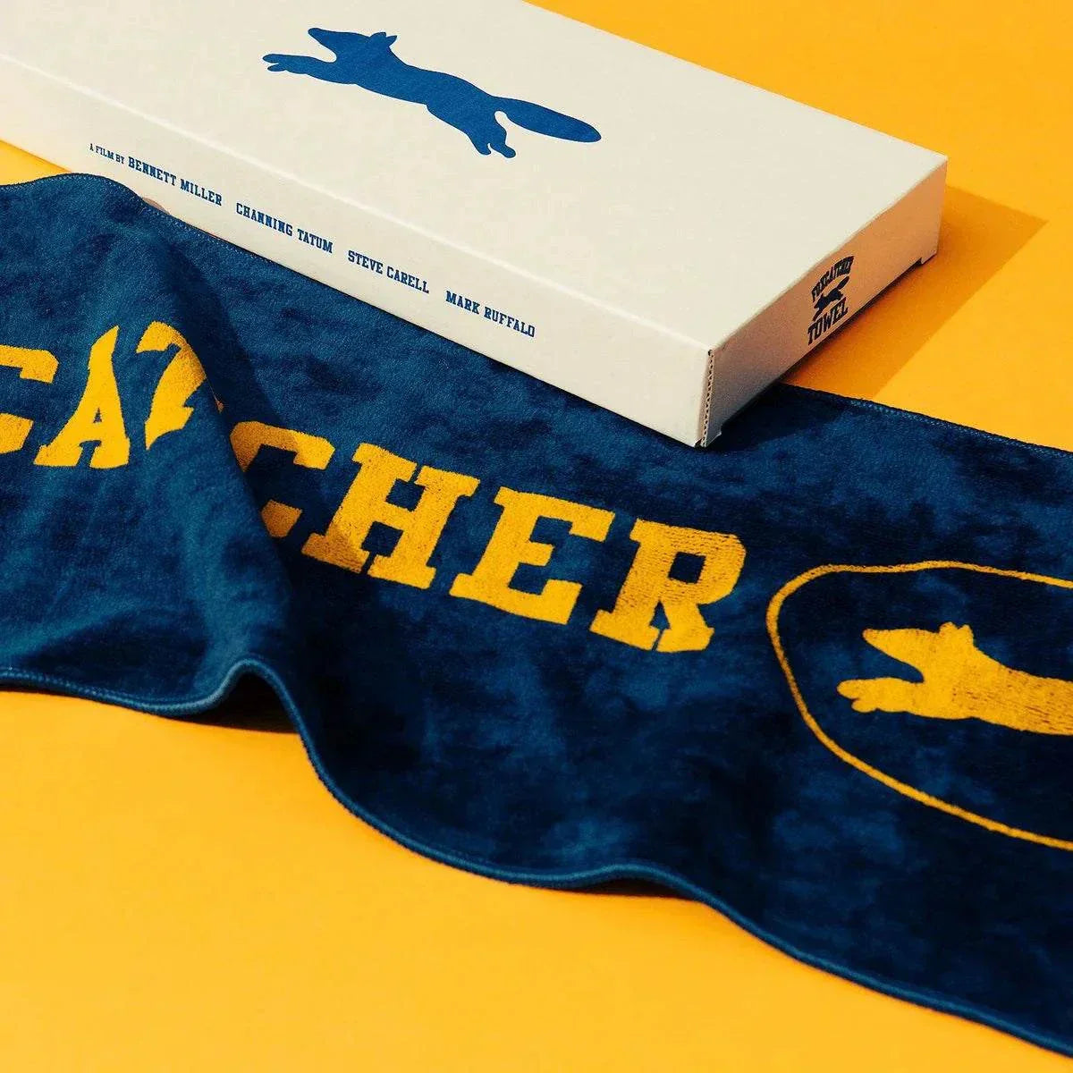Foxcatcher Deluxe Box Blu-ray Steelbook with exclusive artwork, gym towel, and protective slip box on yellow background